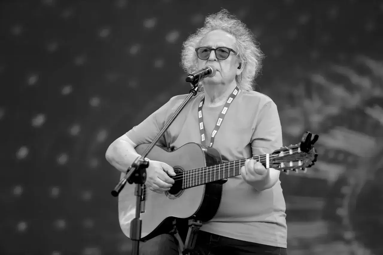 Zegarmistrz światła purpurowy, artysta z gitarą, śpiewa do mikrofonu na tle rozmytych świateł.