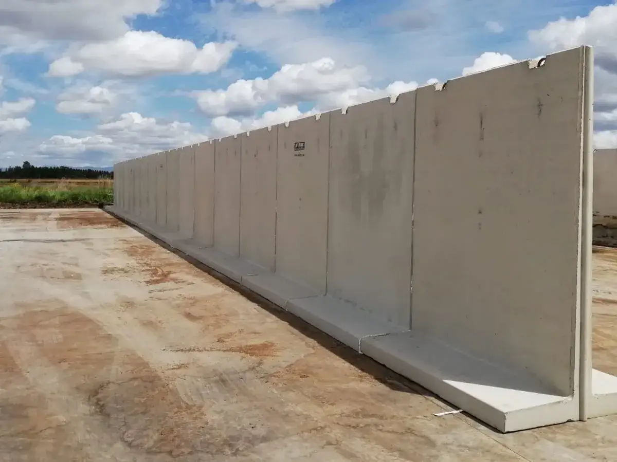 Larga pared de separador de hormig&oacute;n prefabricado, instalada sobre una base de hormig&oacute;n, con un cielo azul y nubes blancas al fondo.