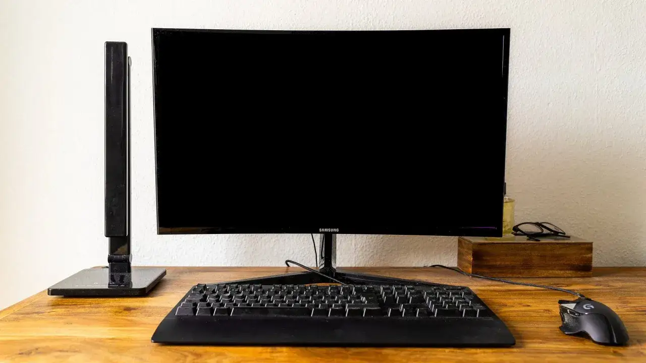 Biurko z czarnym ekranem w laptopie, klawiaturą i myszką. Obok monitora leżą okulary.