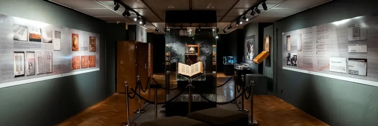 Wnętrze muzeum diecezjalnego w Pelplinie. Centralnie wyeksponowana zabytkowa księga, otoczona gablotami i planszami edukacyjnymi.