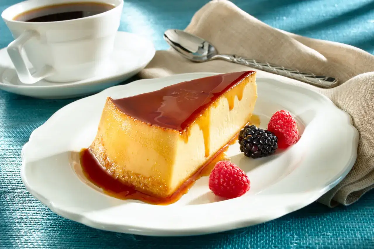 Un delicioso flan de queso con caramelo, acompa&ntilde;ado de frambuesas y moras, junto a una taza de caf&eacute;.