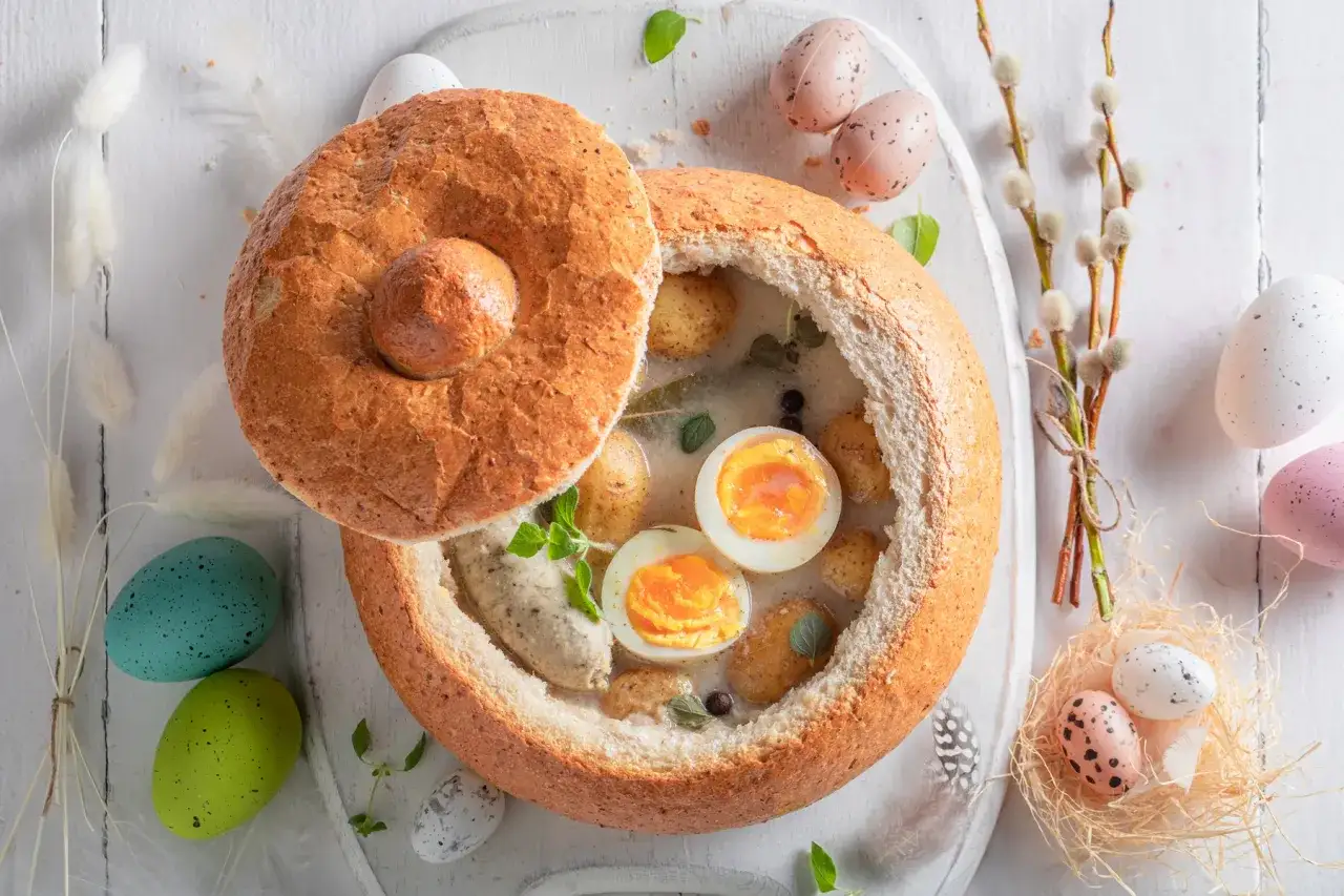 Tradycyjny żurek przepis w chlebie, z jajkiem i ziemniakami, ozdobiony wielkanocnymi pisankami.