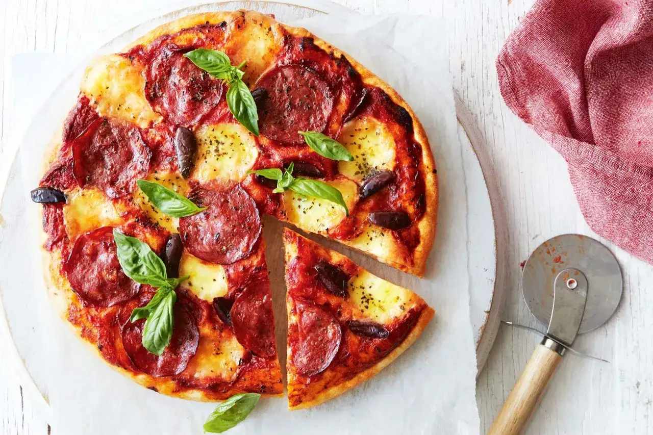 Pyszna pizza salami z oliwkami i bazylią, z jednym kawałkiem odciętym, gotowa do podania.