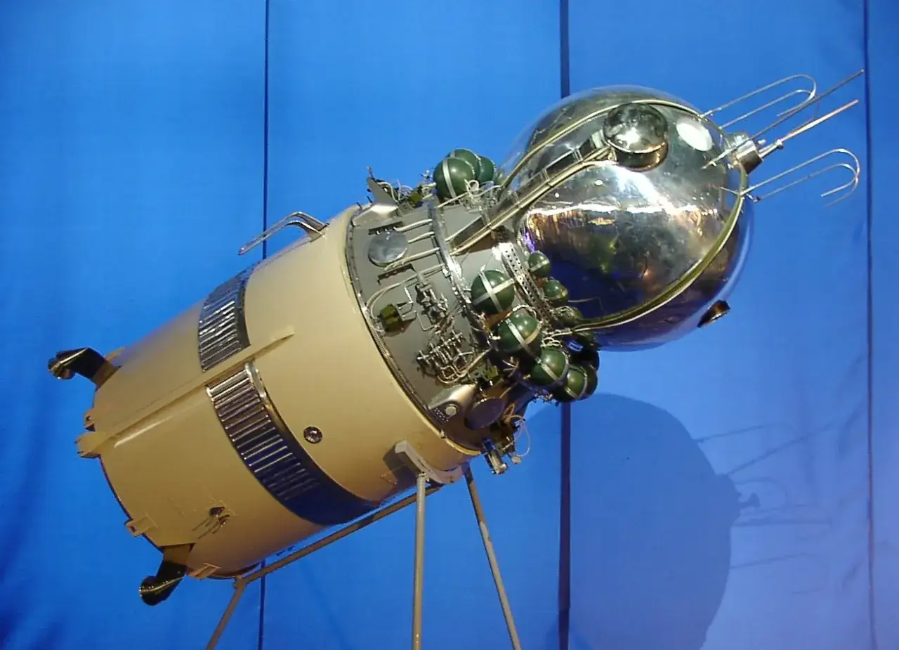Sputnik 1, pierwszy lot w kosmos. Srebrna kapsuła z zielonymi zbiornikami na tle niebieskiego tła.