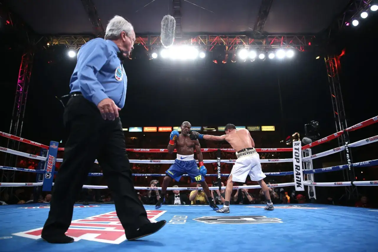 A referee watches intently as two boxers engage in a tense boxing round, with one throwing a punch.