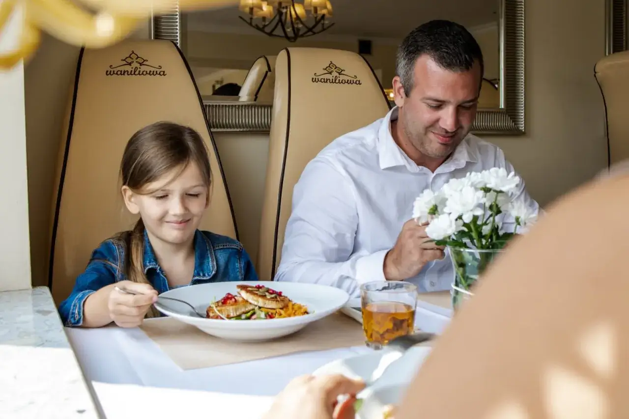Miły dzień brata w restauracji. Dziewczynka i mężczyzna jedzą posiłek, a przed nimi stoi wazon z kwiatami.
