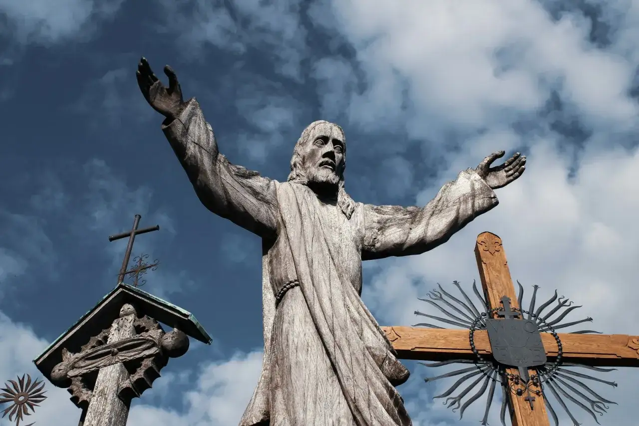 Drewniana figura Jezusa z rozłożonymi ramionami, obok krzyży. Czy masturbacja to grzech ciężki? Pytanie wznosi się ku niebu.