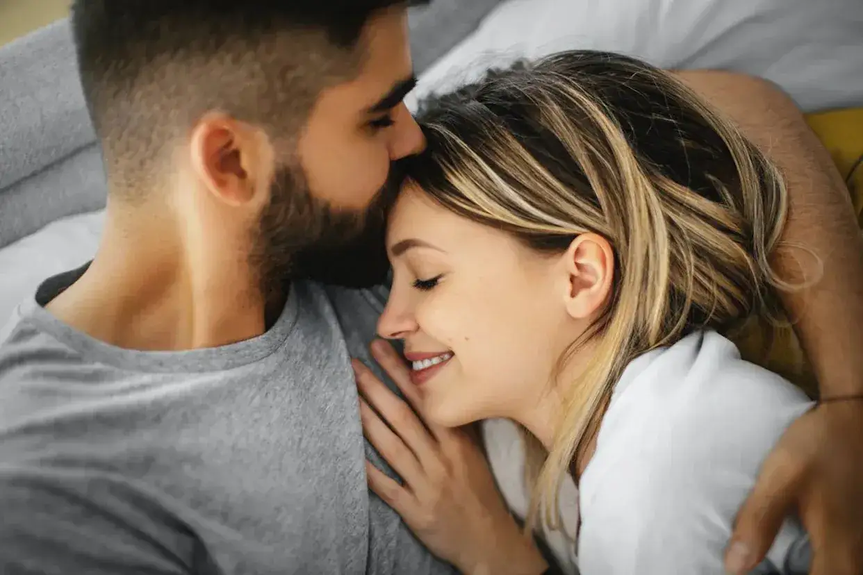 Un homme embrasse le front d'une femme endormie, un moment de tendresse et de câlin amoureux.