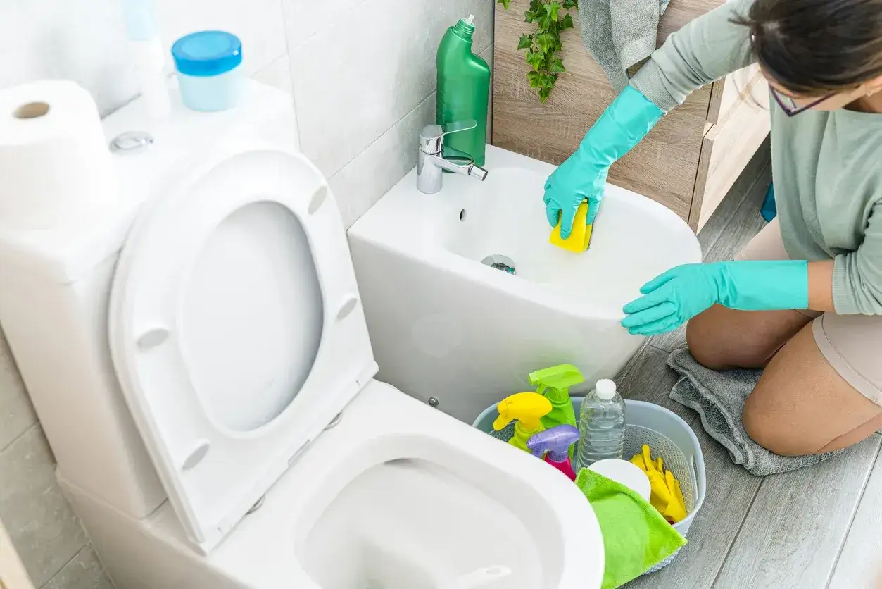 Donna con guanti verdi pulisce il bidet con una spugna gialla, mostrando come sturare il bidet con prodotti per la pulizia a portata di mano.