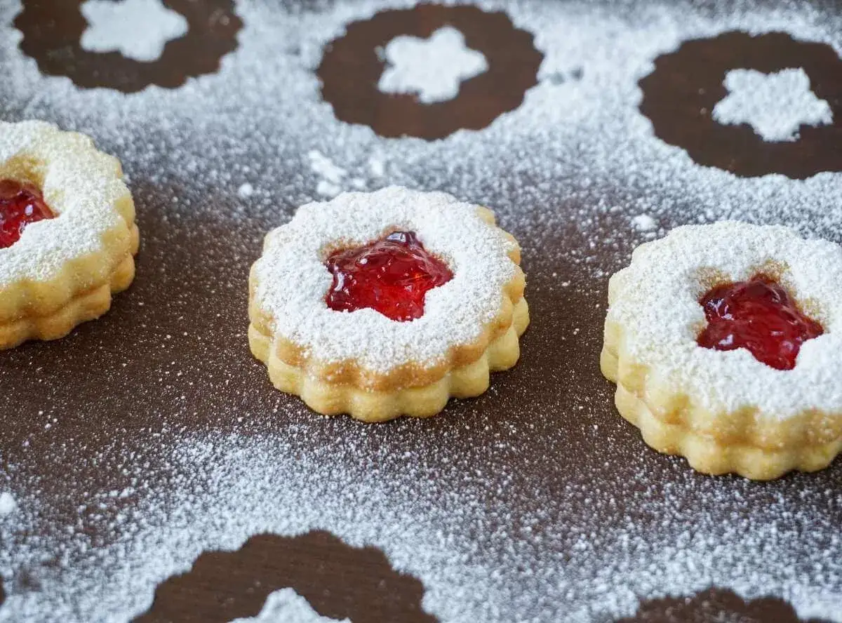 Zwei Schichten zarter Kekse, gef&uuml;llt mit leuchtend roter Marmelade und best&auml;ubt mit Puderzucker. Diese k&ouml;stlichen Kekse mit Marmelade sind ein Genuss.