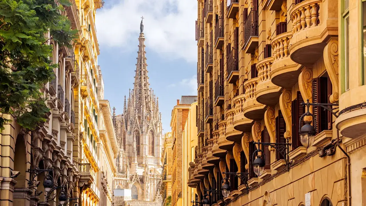 Gotische Kathedrale ragt über sonnenbeschienene Gebäude mit verzierten Balkonen. Ein Blick auf die Barcelona Attraktionen.