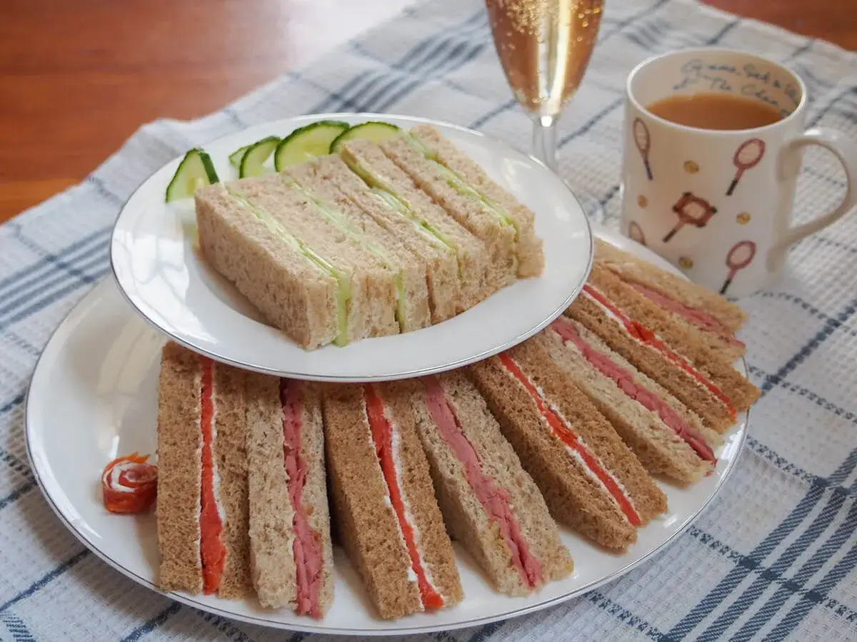 Deliciosos s&aacute;ndwiches de pepino y jam&oacute;n, listos para la hora del t&eacute; en Inglaterra. Una taza de t&eacute; y una copa de champ&aacute;n completan la escena.