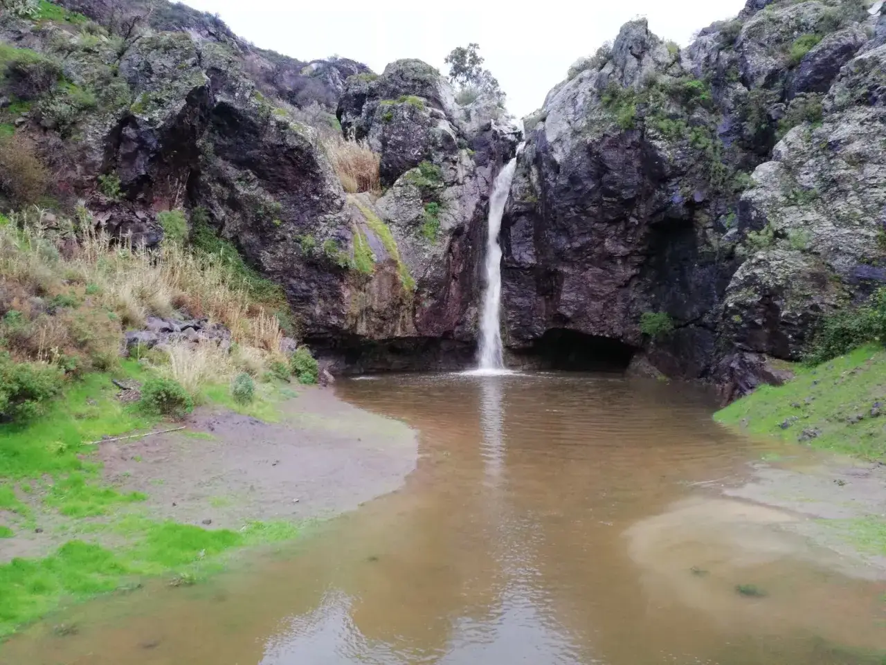 Cascada cayendo en el charco de la paloma, rodeado de rocas y vegetaci&oacute;n.