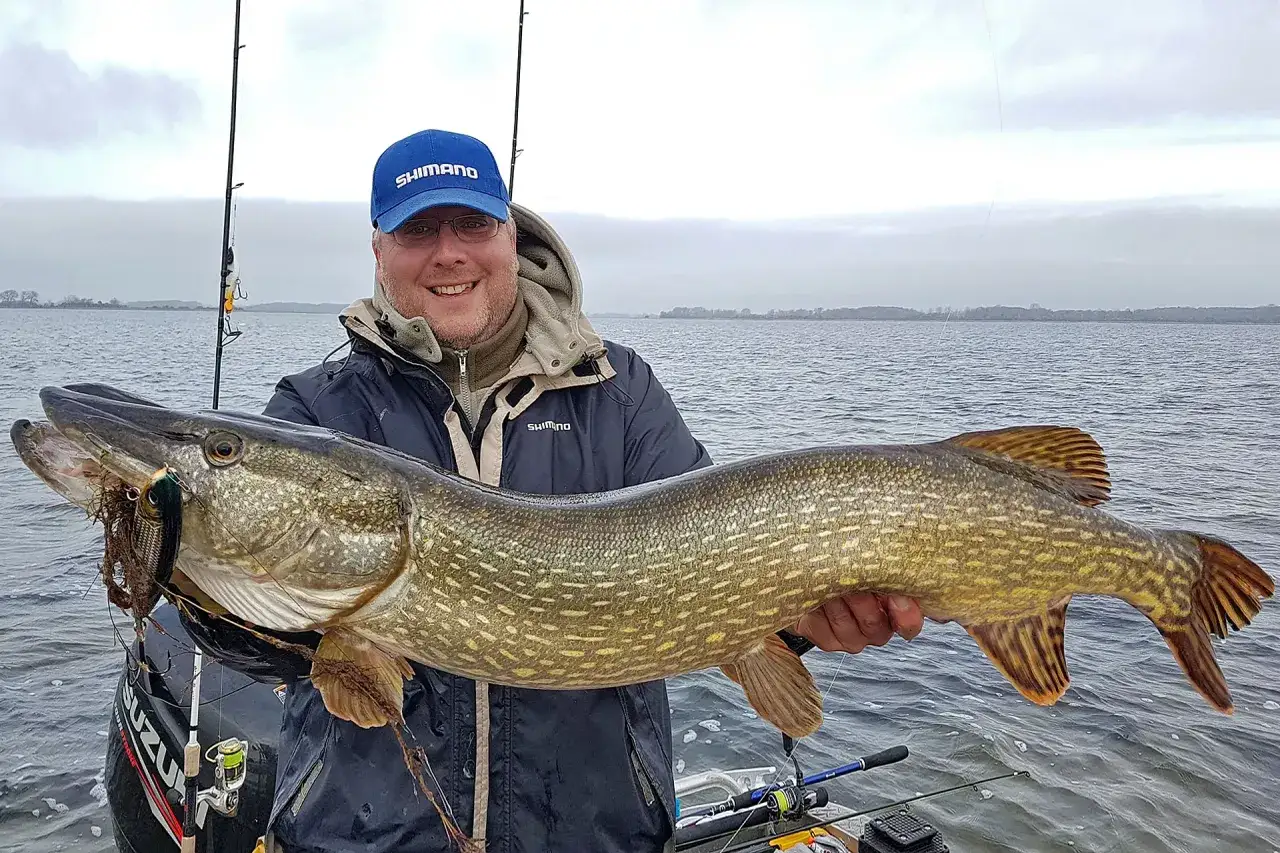 Gl&uuml;cklicher Angler h&auml;lt riesigen Hecht, gefangen mit gro&szlig;en K&ouml;dern.