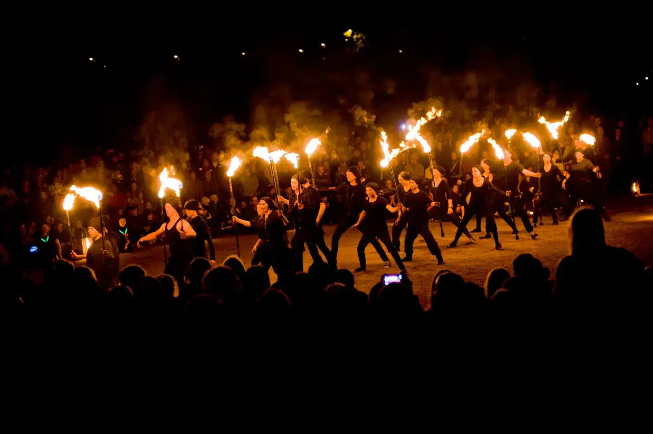 En grupp dansare med facklor lyser upp natten under Uppsala kultur natt. Publiken ser p&aring;.