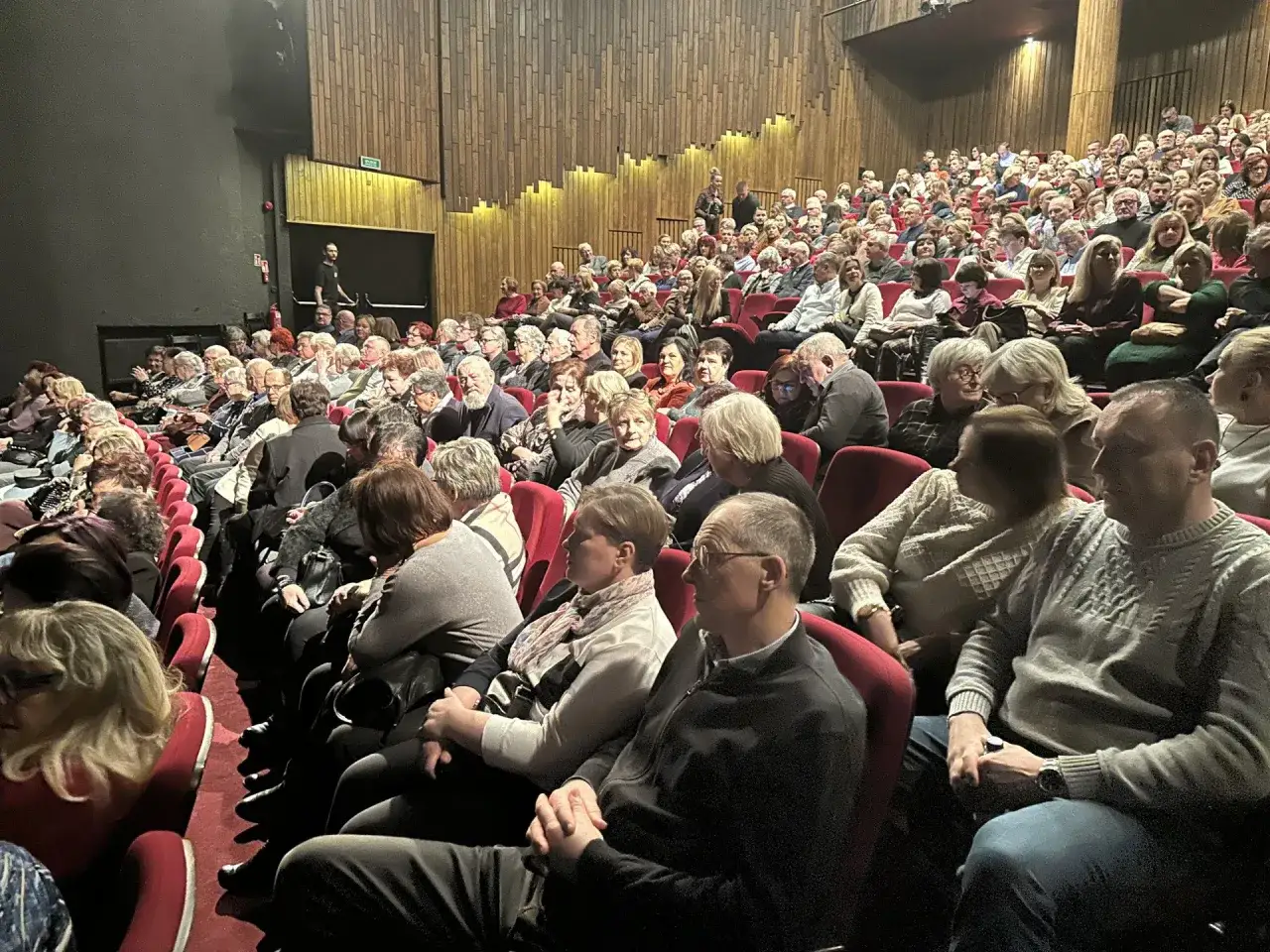 Widownia w Teatrze Capitol Poznań, ludzie siedzą w czerwonych fotelach, słuchając występu.