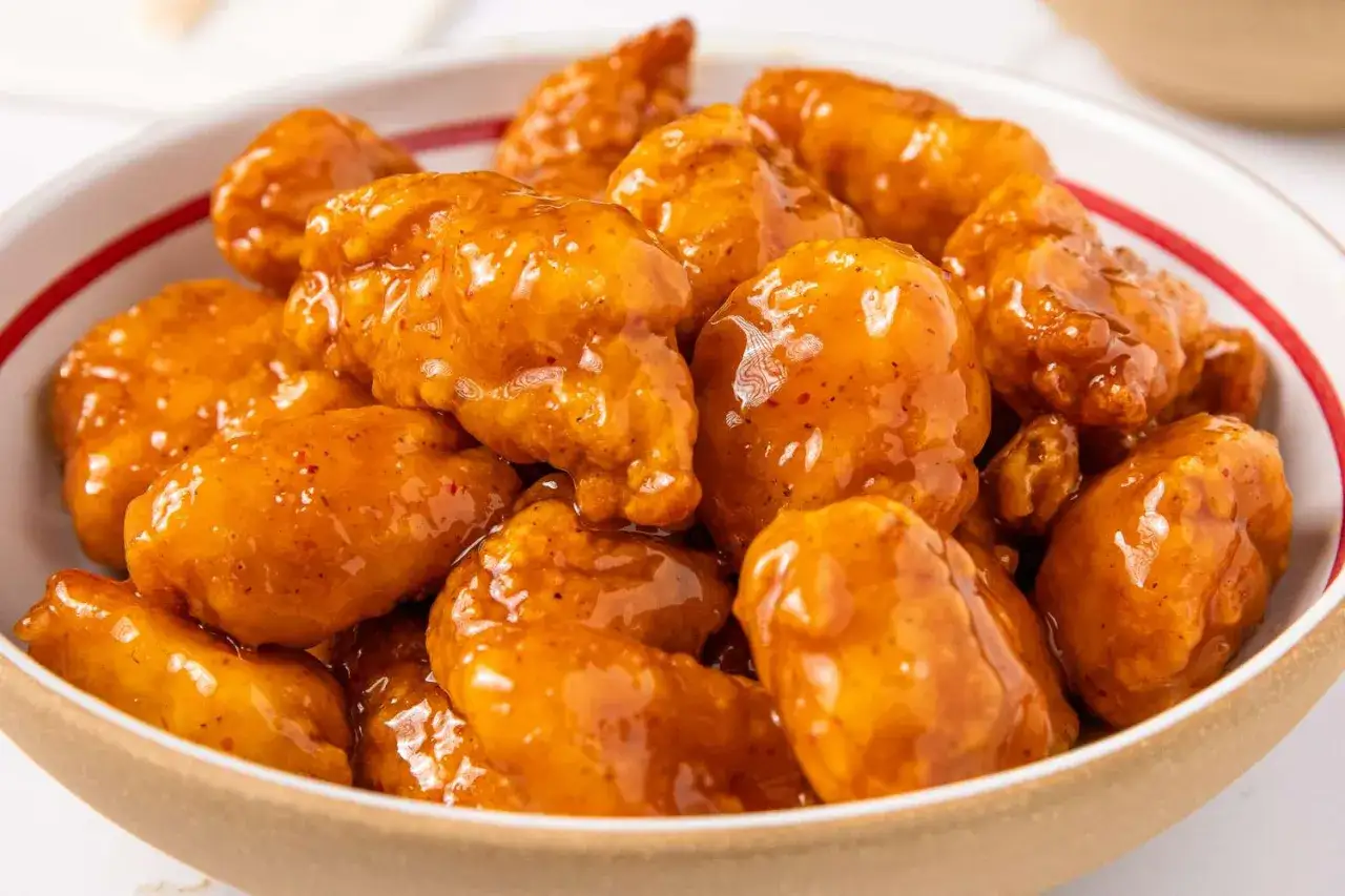 Trozos de pollo a la naranja glaseados y brillantes, servidos en un cuenco.