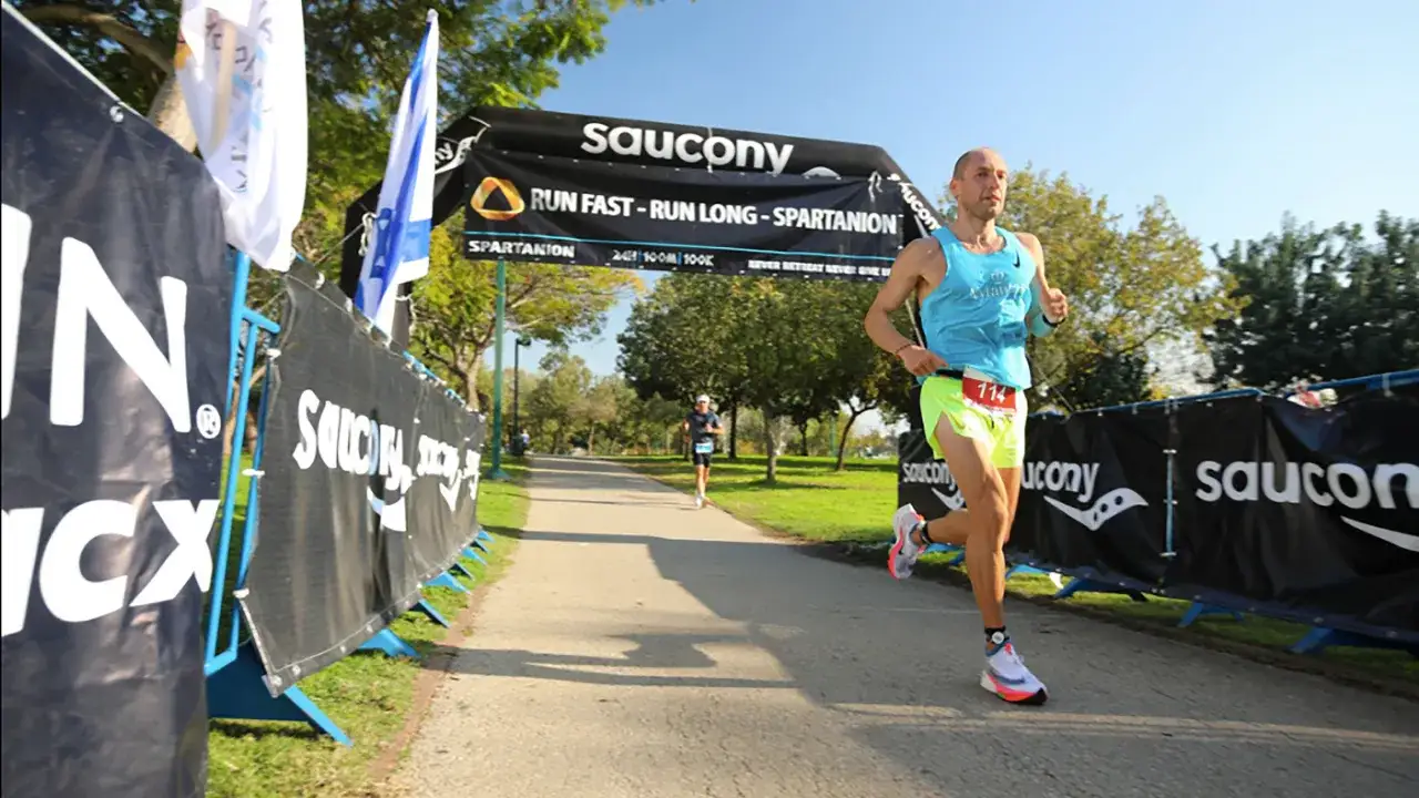 Läufer mit Startnummer 114 auf dem Weg zum ultramarathon weltrekord. Saucony-Banner säumen die Strecke.