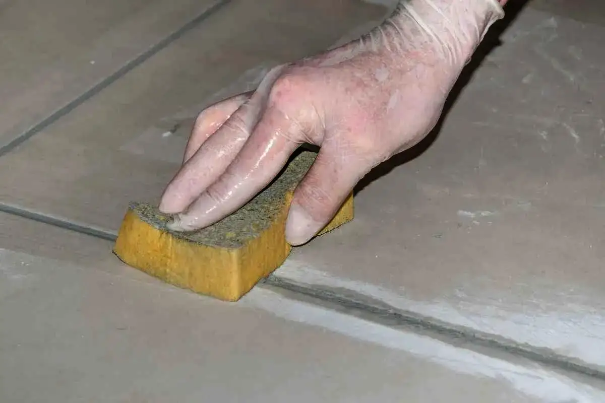 Mano con guanto che pulisce le fughe di un pavimento con una spugna, per rifare le fughe dei pavimenti.