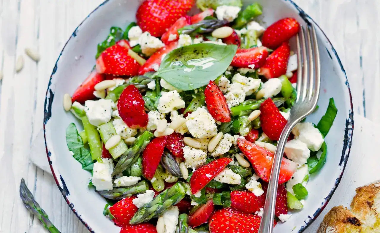 Frischer Spargel-Salat mit Erdbeeren, Feta und Pinienkernen in einer Schüssel, garniert mit Basilikum.
