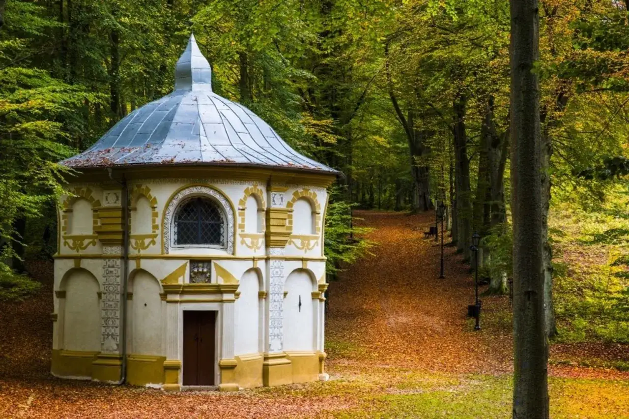 Kaplica na Kalwarii Wejherowskiej otoczona jesiennym lasem. Ścieżka wysypana liśćmi prowadzi do kolejnych stacji.