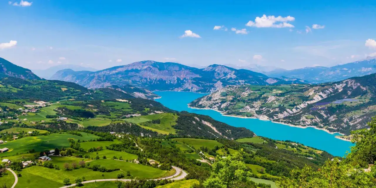 Vue panoramique depuis le pic de Morgon sur un lac turquoise entouré de montagnes verdoyantes et de champs.