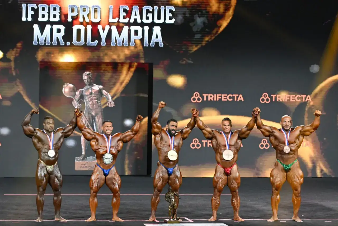 F&uuml;nf Bodybuilder mit Medaillen auf der B&uuml;hne des Mr. Olympia. Die Frage 