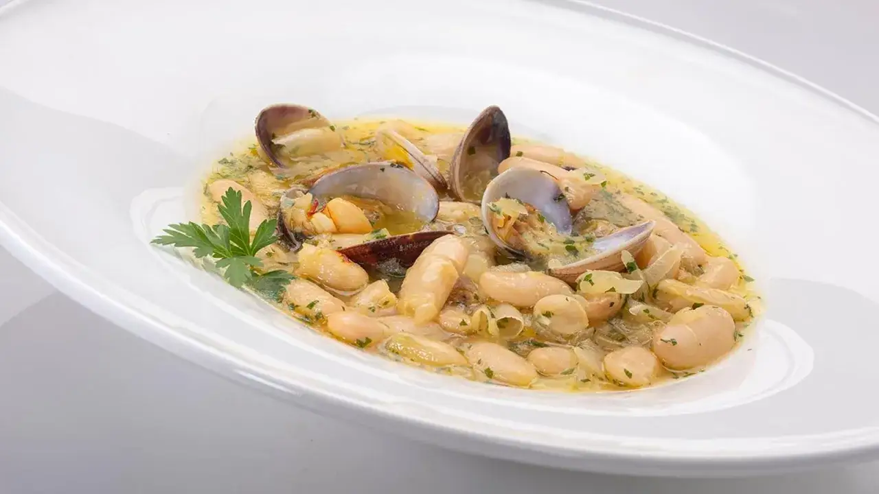 Un plato de fabes con almejas, con jud&iacute;as blancas tiernas y almejas en una salsa sabrosa, adornado con perejil fresco.