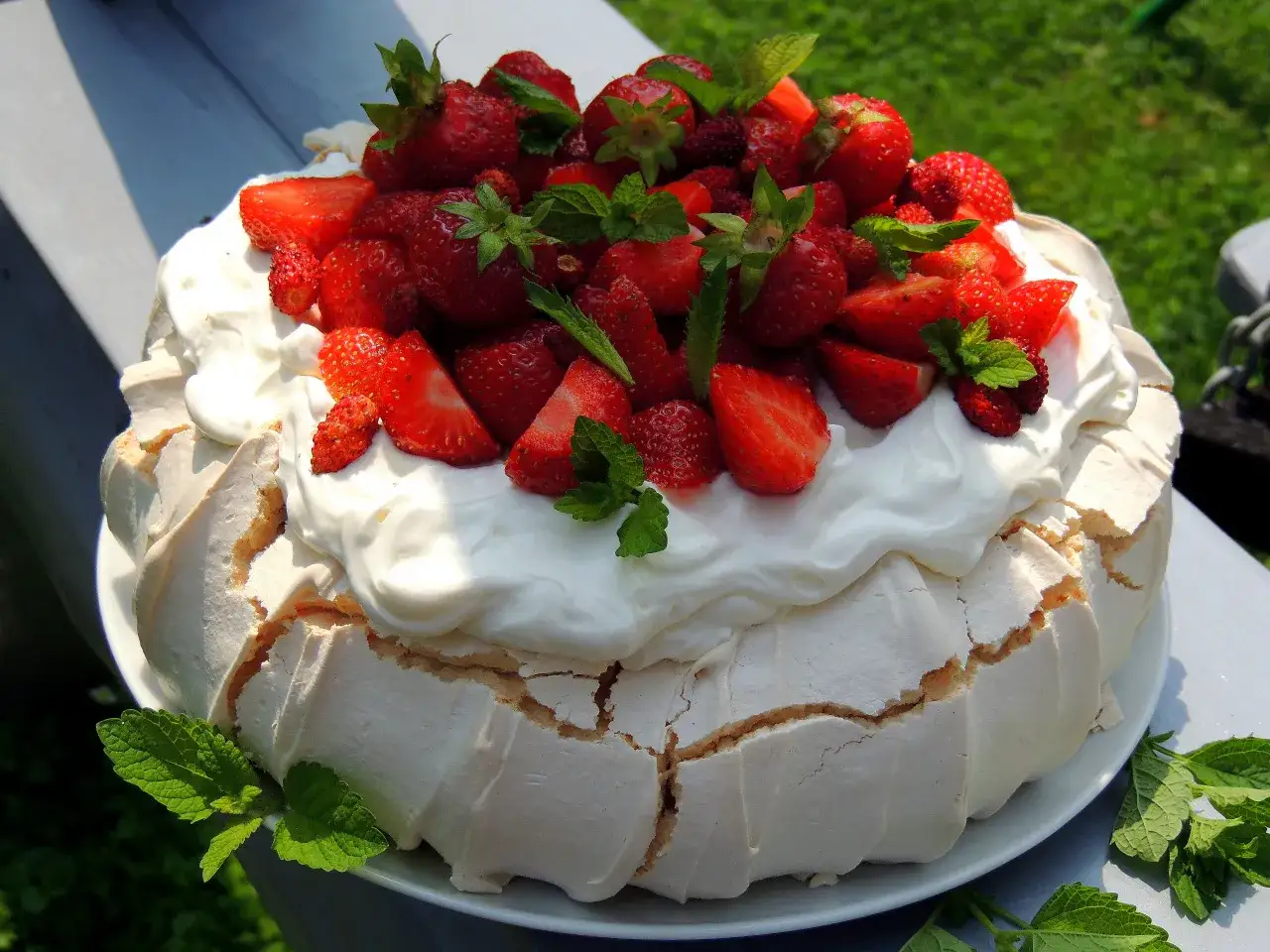 Letni tort bezowy Pavlova, obficie udekorowany bitą śmietaną i świeżymi truskawkami, z listkami mięty.