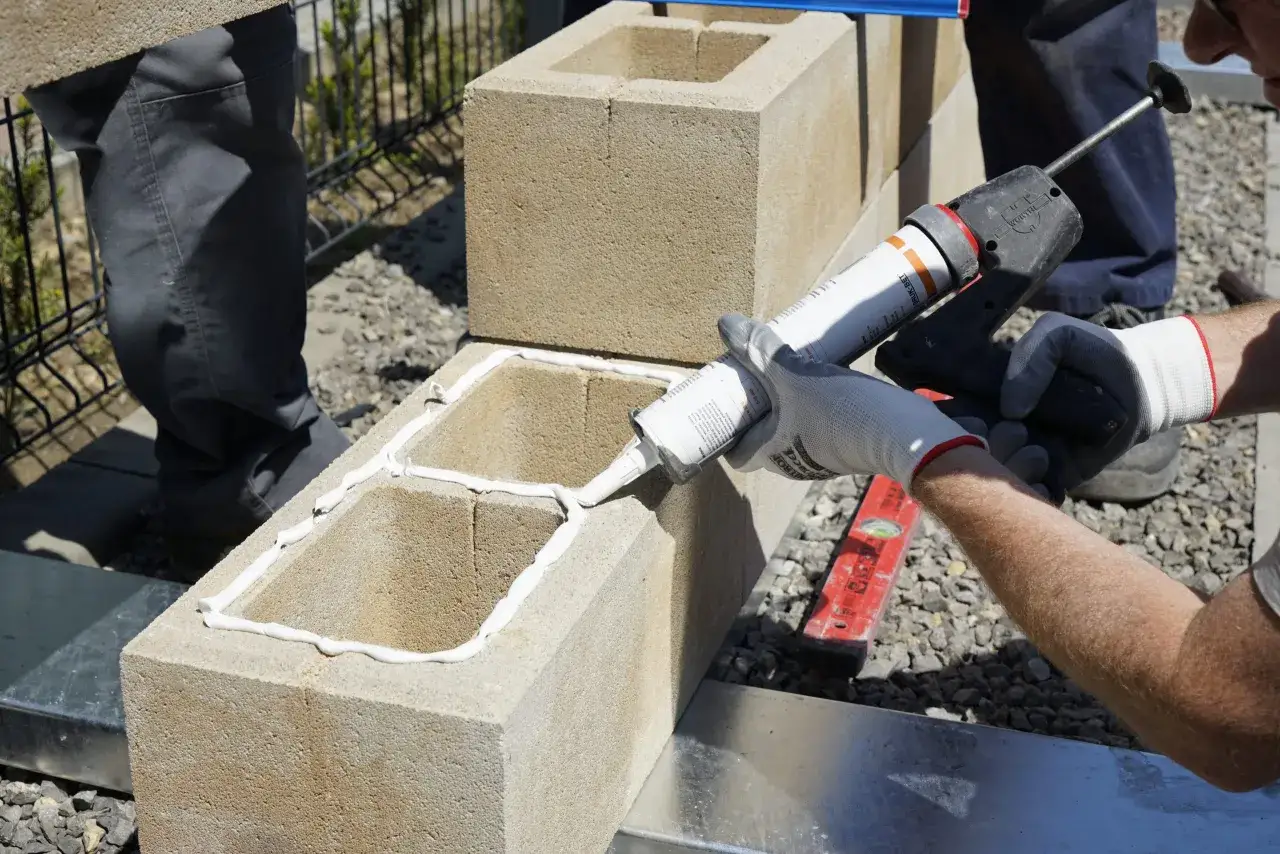 Praca przy budowie ogrodzenia z bloczków betonowych. Nakładanie masy uszczelniającej na bloczki. Cena za mb robocizny zależy od materiału i skomplikowania.
