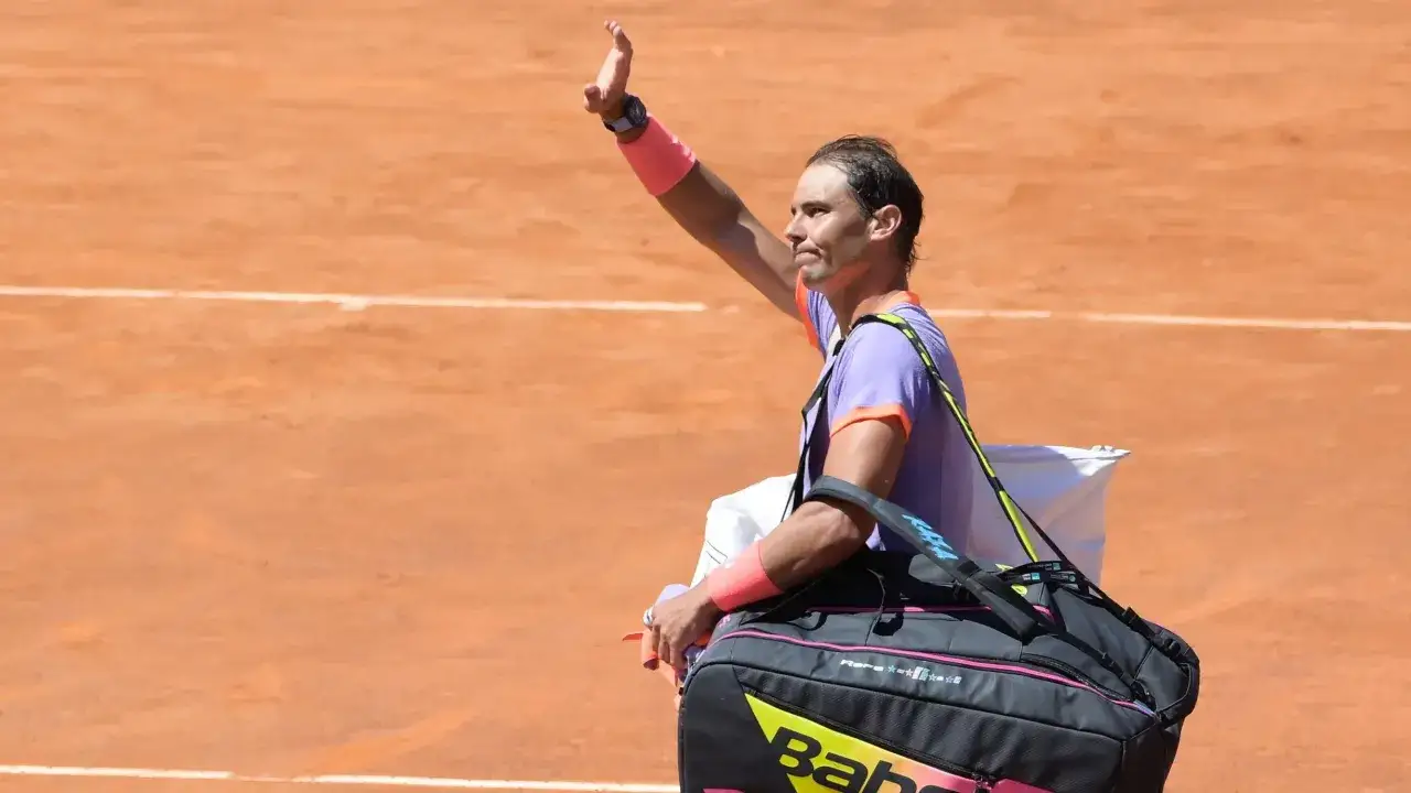Rafael Nadal, imię nadane przez kibiców, macha do publiczności na korcie ziemnym, niosąc torbę tenisową.