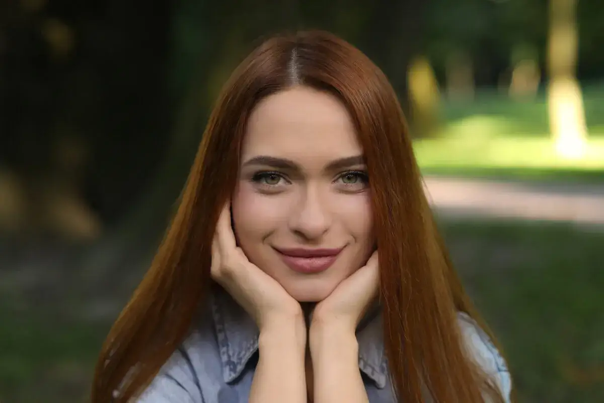 Uśmiechnięta kobieta z rudymi włosami, które przywodzą na myśl odcień rudego brązu.
