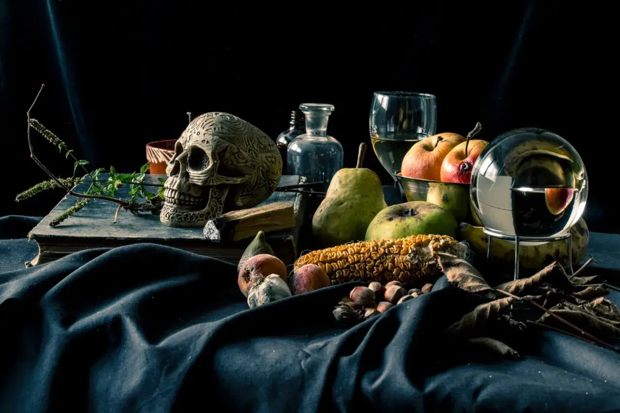 Scatti still life: teschio decorato, frutta, mais, noci e una sfera di cristallo su un drappo scuro.