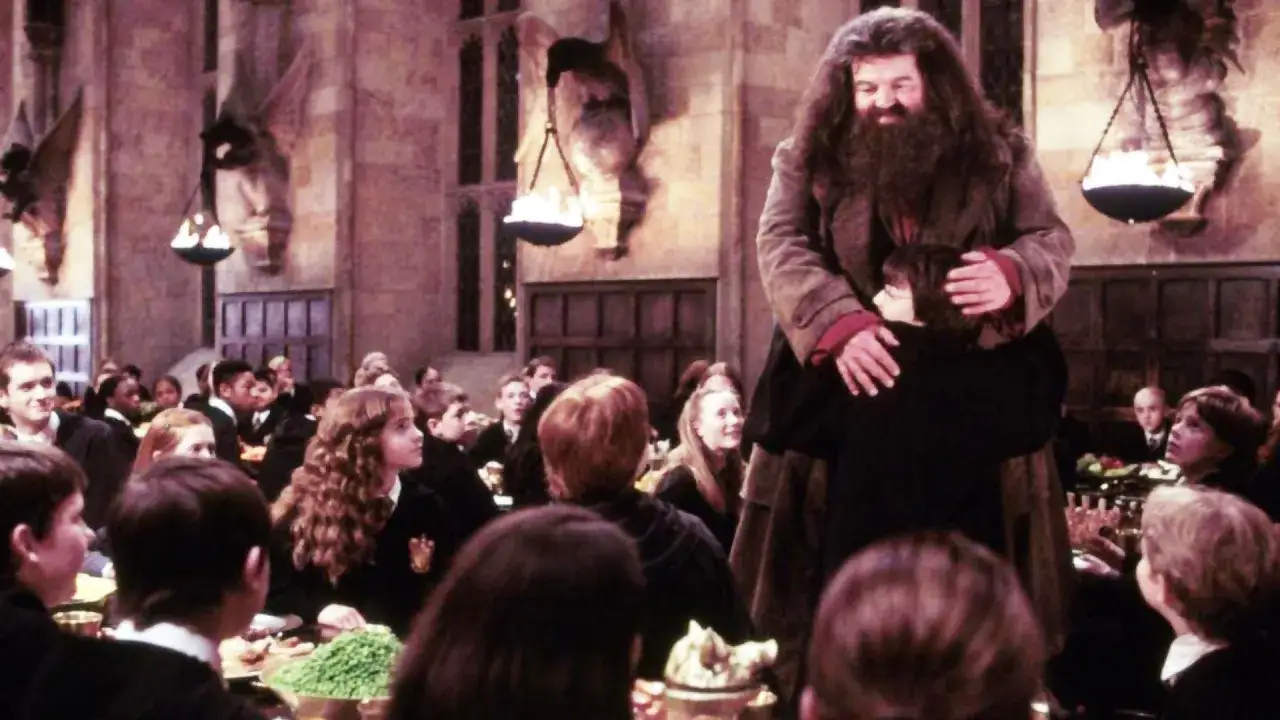 Hagrid aktor obejmuje Harry'ego w Wielkiej Sali. Wokół siedzą uczniowie Hogwartu.