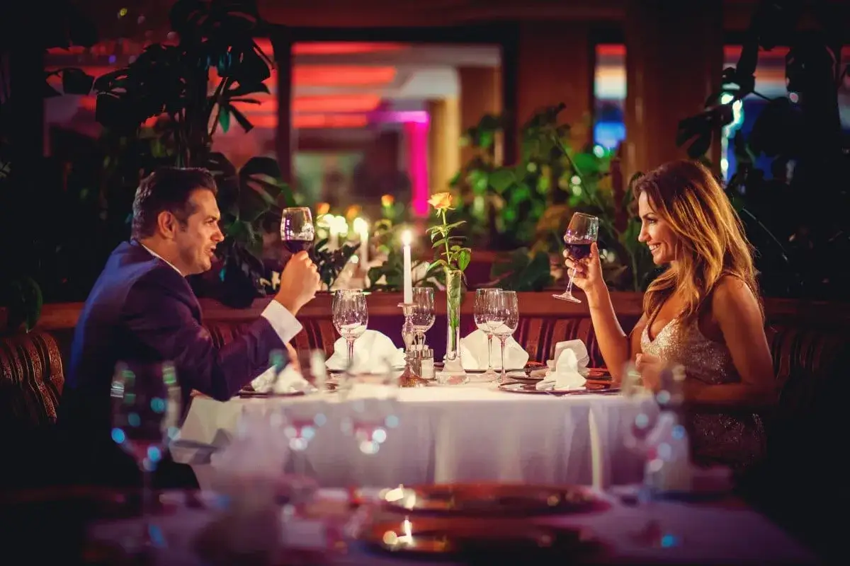 Elegancka para wznosi toast kieliszkami wina podczas romantycznej kolacji. Zastanawiasz się, ile kosztuje doba w hotelu Gołębiewski dla dwóch?