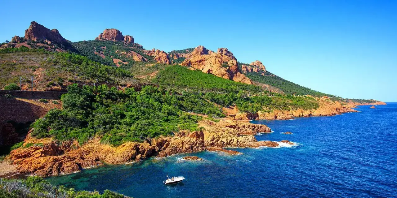 La c&ocirc;te rocheuse rouge de Saint-Rapha&euml;l, baign&eacute;e par la mer M&eacute;diterran&eacute;e, avec une petite bateau naviguant dans les eaux bleues.