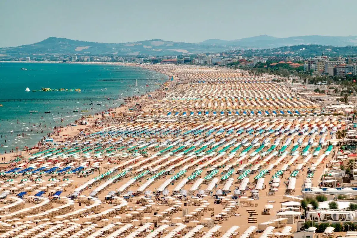 Un'immensa spiaggia a Rimini, con file ordinate di ombrelloni colorati e bagnanti che si godono il sole e il mare Adriatico.