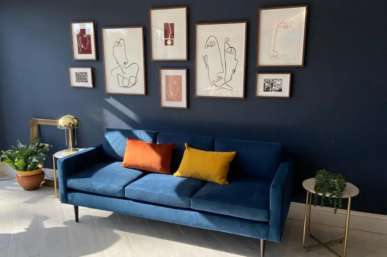 Ein tiefblaues Sofa mit passender Wandfarbe, umrahmt von abstrakter Kunst. Orange und gelbe Kissen setzen Akzente.