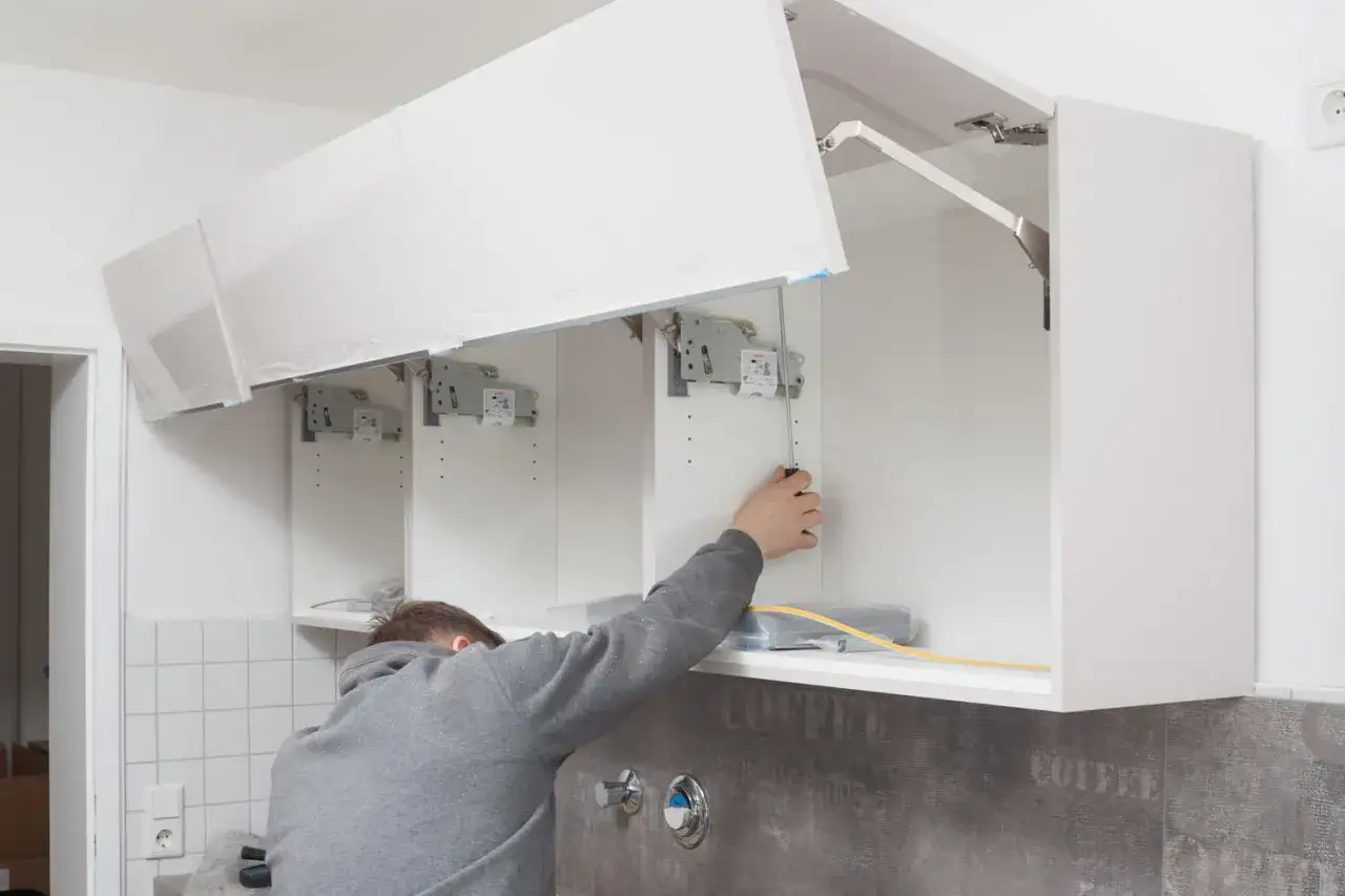 Mann befestigt die **Theke auf Arbeitsplatte** mit Schrauben. Oben sind weiße Küchenschränke montiert.