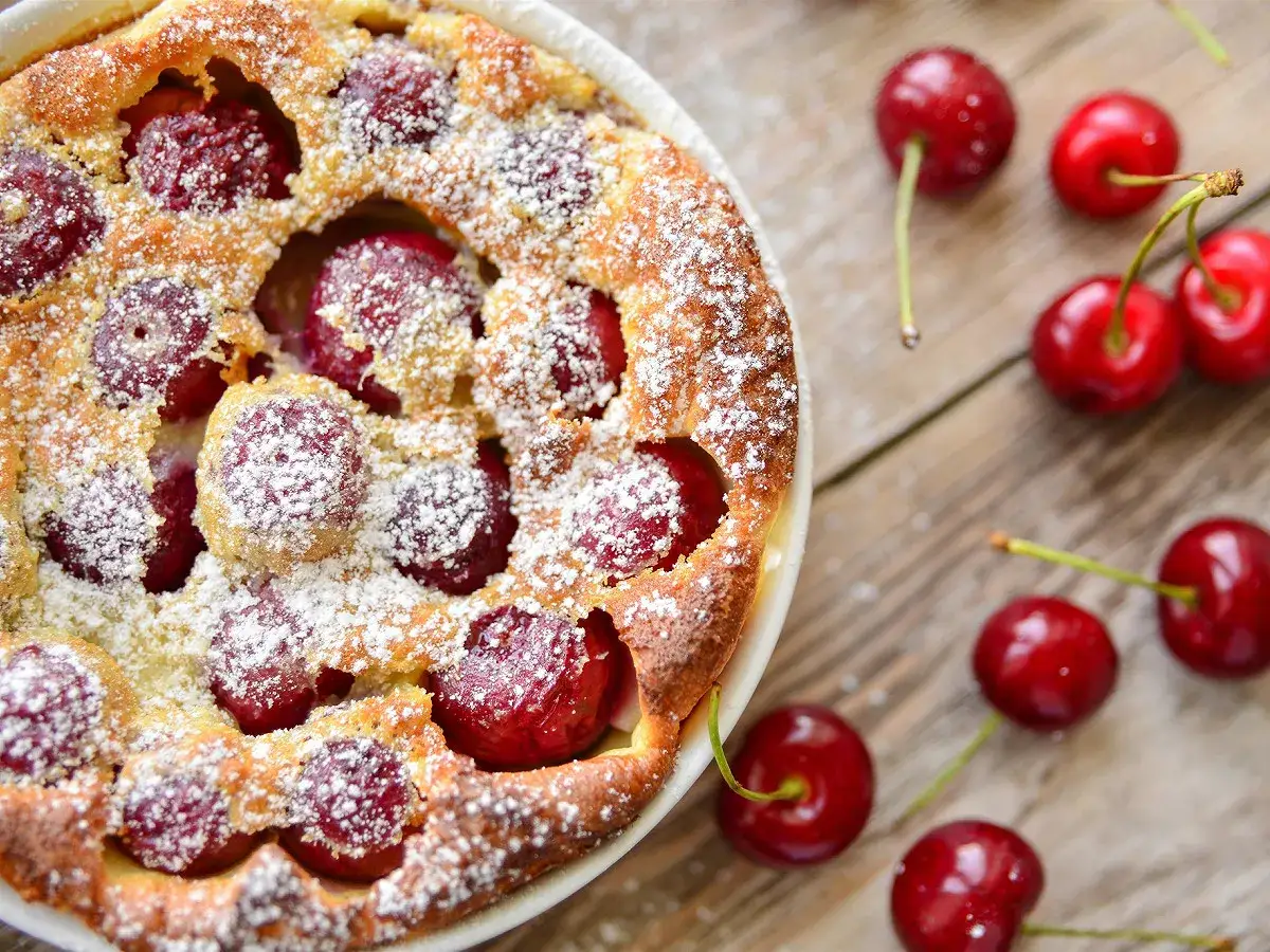 Un délicieux clafoutis aux cerises congelées, saupoudré de sucre glace, sur fond de bois rustique.