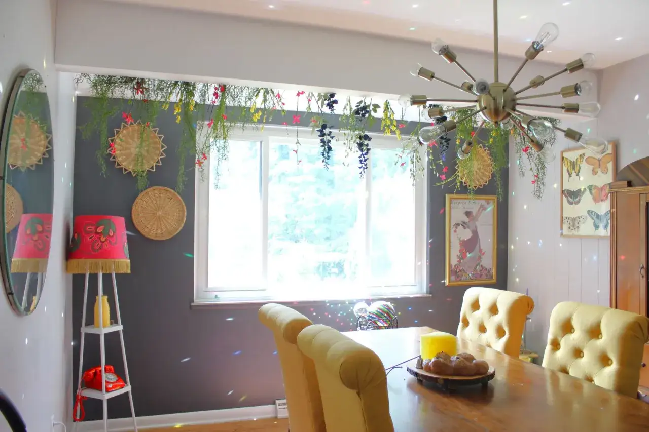 Gr&uuml;ne Ranken und bunte Blumen schm&uuml;cken die Gardinenstange &uuml;ber dem Fenster. Ein Spiegel und ein auff&auml;lliger Kronleuchter vervollst&auml;ndigen die Dekoration.