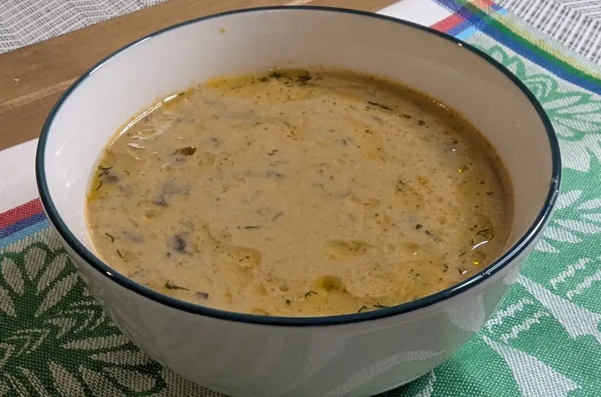 Kremowa zupa z selera naciowego, doprawiona ziołami, w białej misce na kolorowym obrusie.