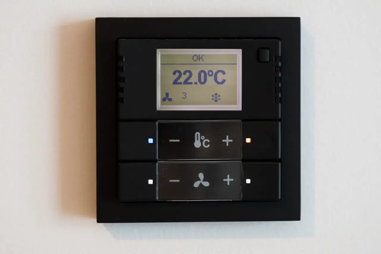 Panel sterowania klimatyzacją w hotelu: wyświetla 22°C, ikony wentylatora i płatka śniegu. Przyciski do regulacji temperatury i nawiewu.