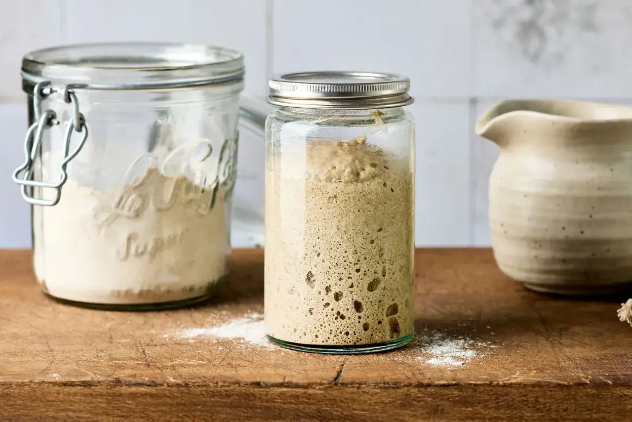Ein Glas mit aktivem Sauerteig, der Blasen wirft. Daneben ein Glas mit Mehl. Der Sauerteig verdoppelt sich nicht, aber er lebt!