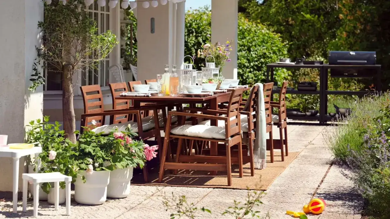 Gemütliche Terrasse gestalten mit wenig Geld: Holztisch mit Stühlen, Grill und Pflanzen laden zum Verweilen ein.