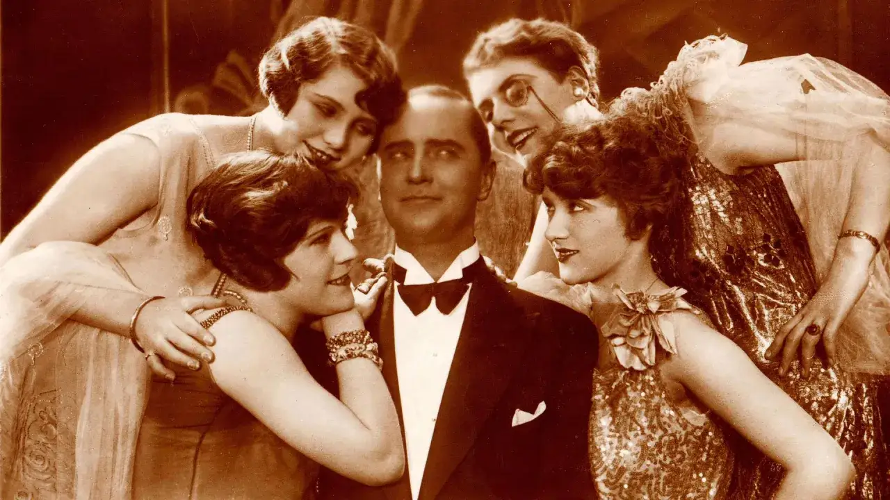 Ein Mann im Smoking, umgeben von vier Frauen in glamour&ouml;sen Kleidern. Eine Szene, die an das pulsierende Leben im Berlin der 1920er Jahre erinnert.