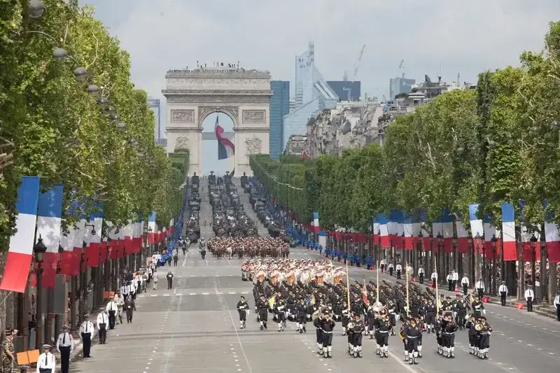 Parada wojskowa w Paryżu z okazji święta narodowego. W tle Łuk Triumfalny, a na ulicy flagi Francji. To jest właśnie lipiec po francusku!