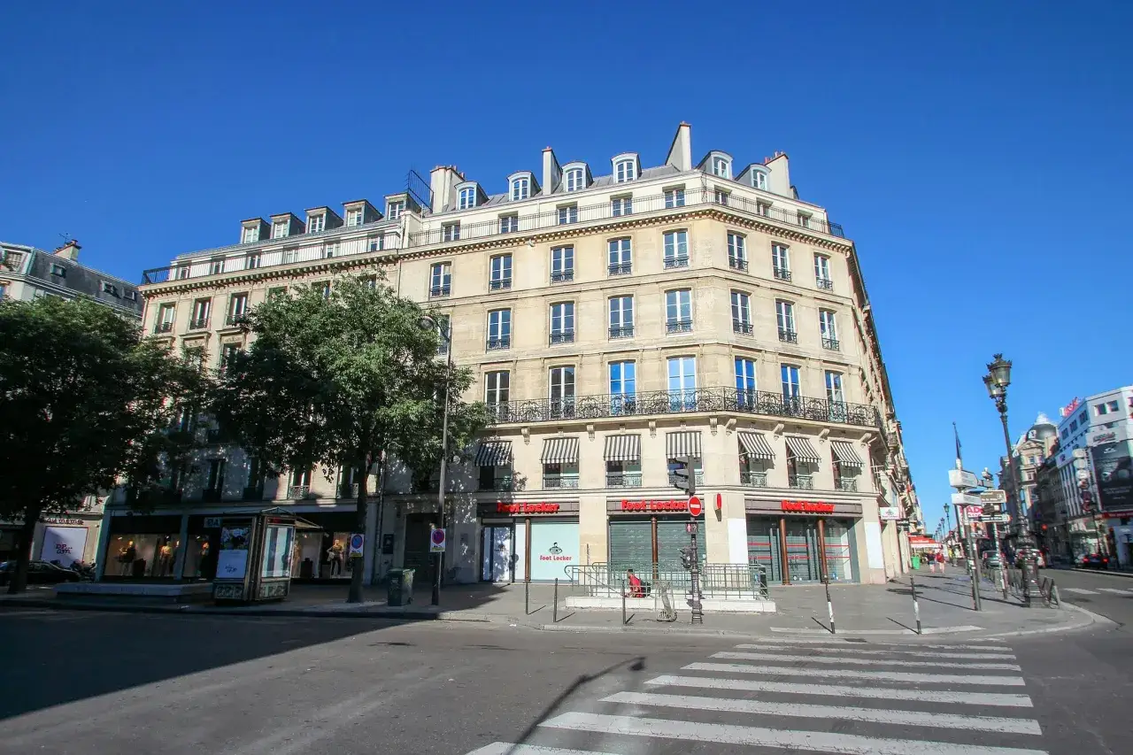 Elegancki budynek z mansardowym dachem przy rue de Rivoli w Paryżu, z markizami nad oknami i sklepem Foot Locker na parterze.