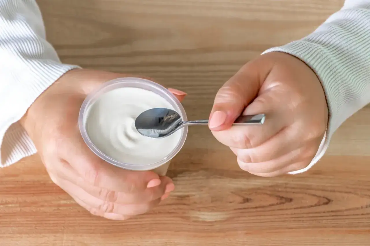 Ręce trzymają kubek ze skyr. Czy skyr jest lekkostrawny? Tak, jest to produkt bogaty w białko i łatwo przyswajalny.