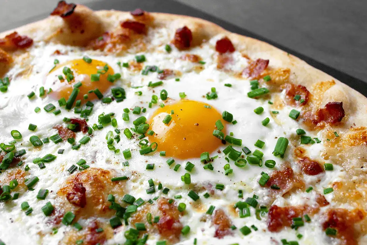 Pizza carbonara avec &oelig;ufs au plat, lardons croustillants et ciboulette fra&icirc;che. Un d&eacute;lice pour les yeux et les papilles.